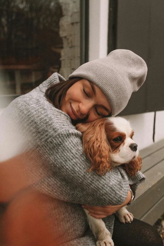 a woman in a hat hugs her brown and white dog