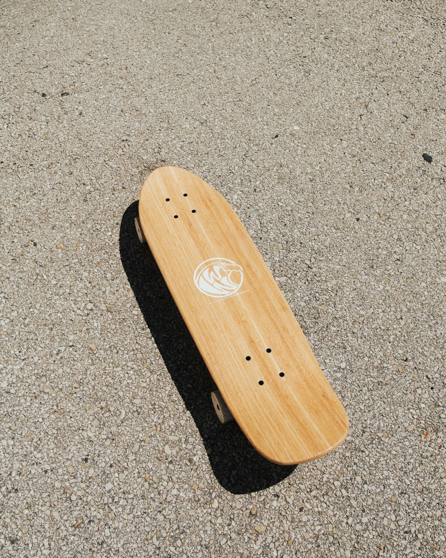 the skateboard is laying on the pavement and casting a shadow