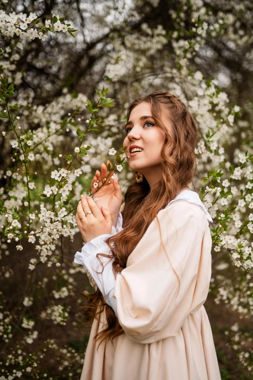 a pretty young lady standing under a tree with white flowers