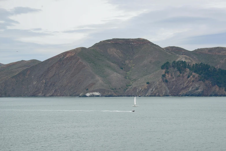 a sail boat floating along the water with large hills in the background