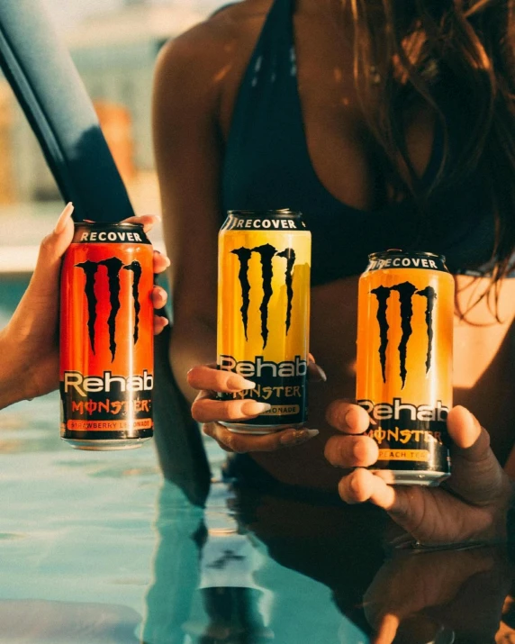 a woman is showing off three monster energy drinks