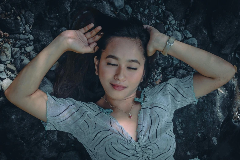 a beautiful young woman wearing a necklace standing next to rocks