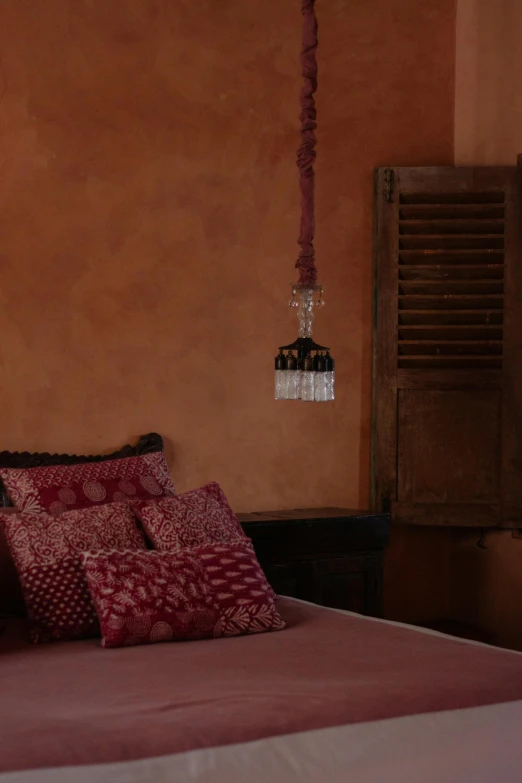 a bed with two red pillows, a wooden armoire and a hanging light fixture