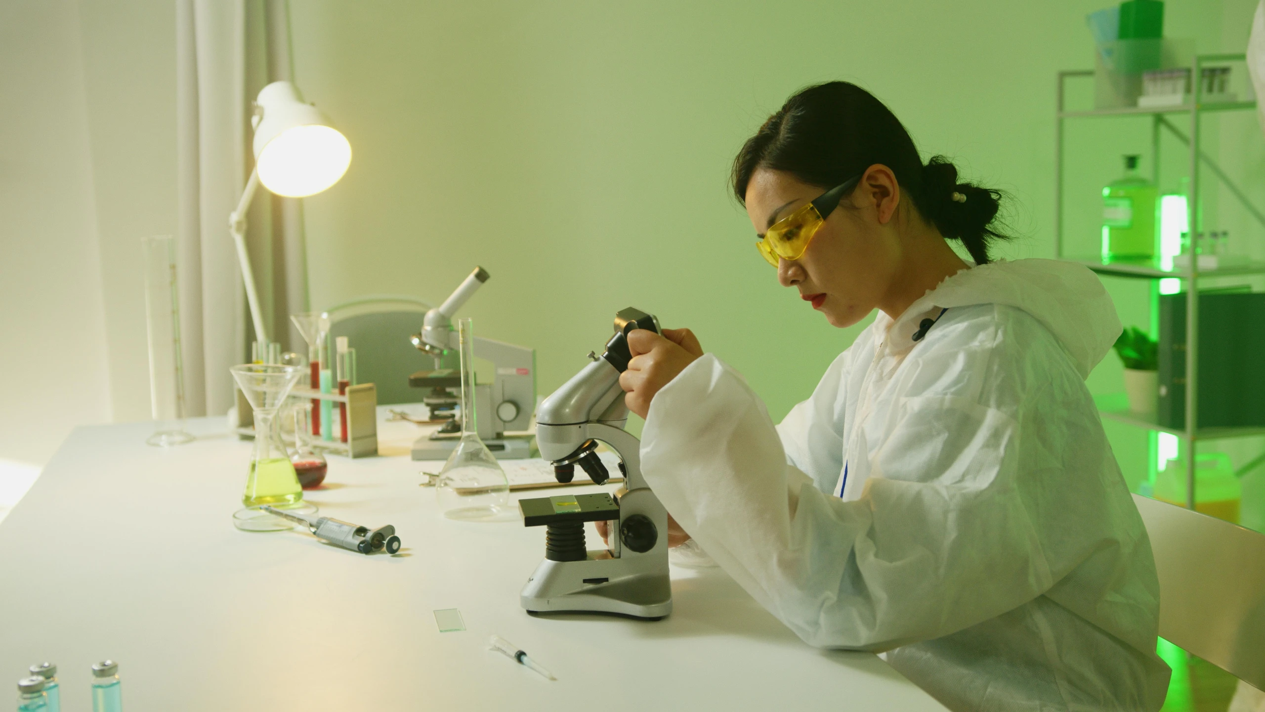 a woman in a lab coat sitting at a table with a microscope