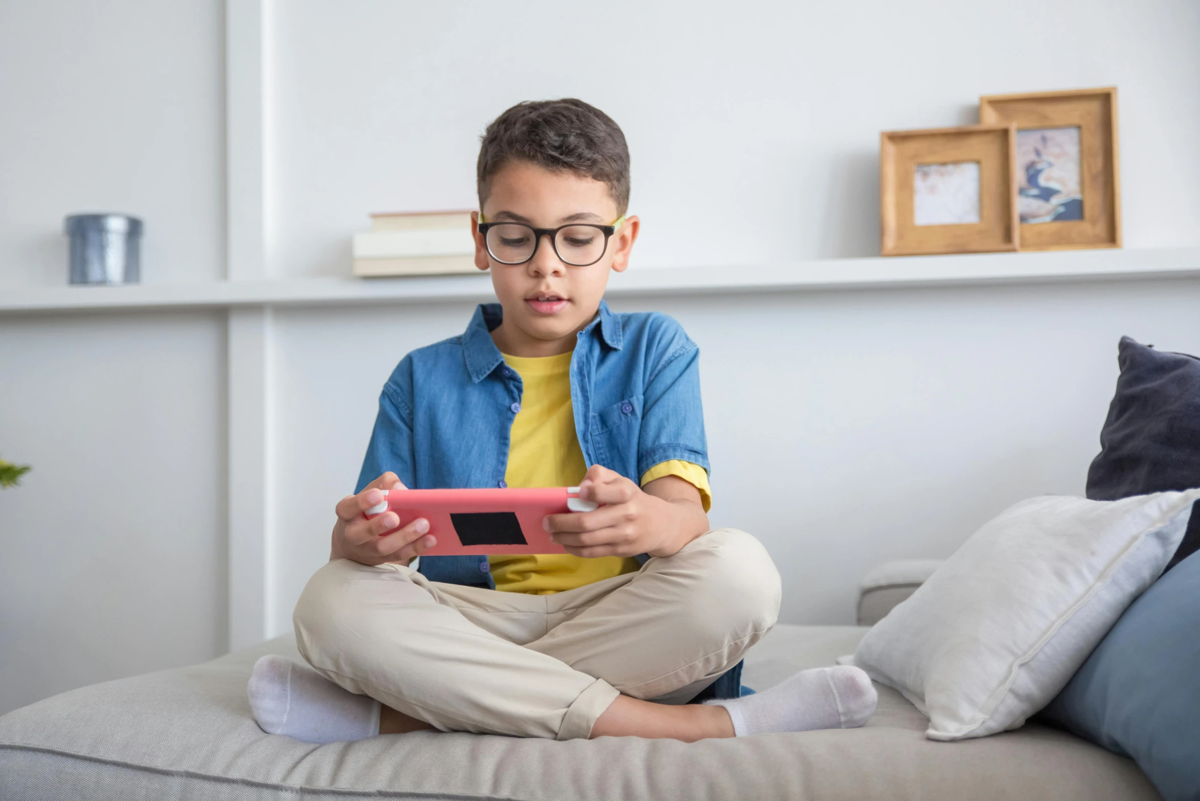 a little boy that is sitting on a bed looking at an electronic device