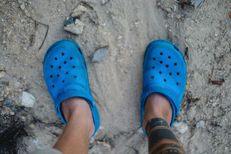 legs in shoes on beach, with rocks in background