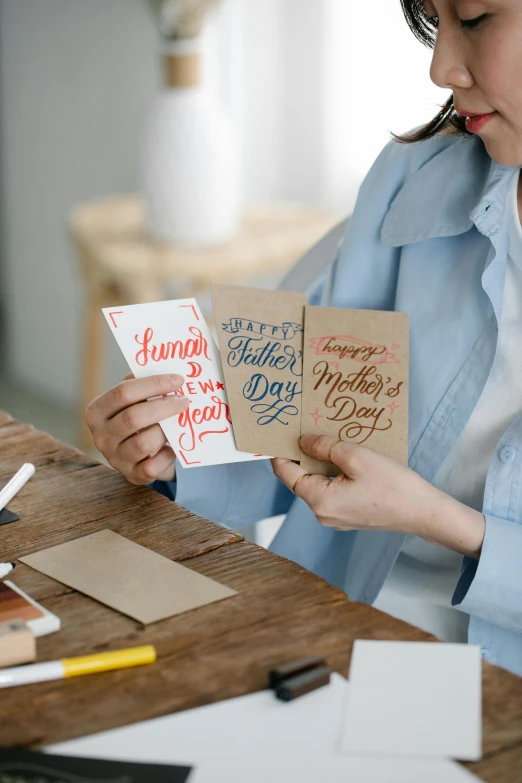 a woman holding two greeting cards over a crafting table