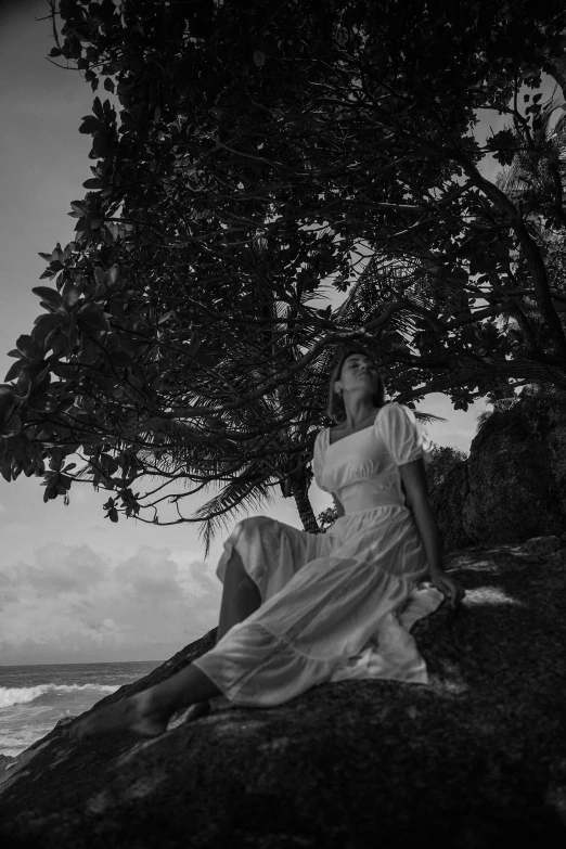 the woman in white is sitting on the rock by the water