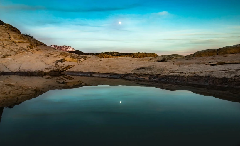 a reflection of the rocks and the moon in a river