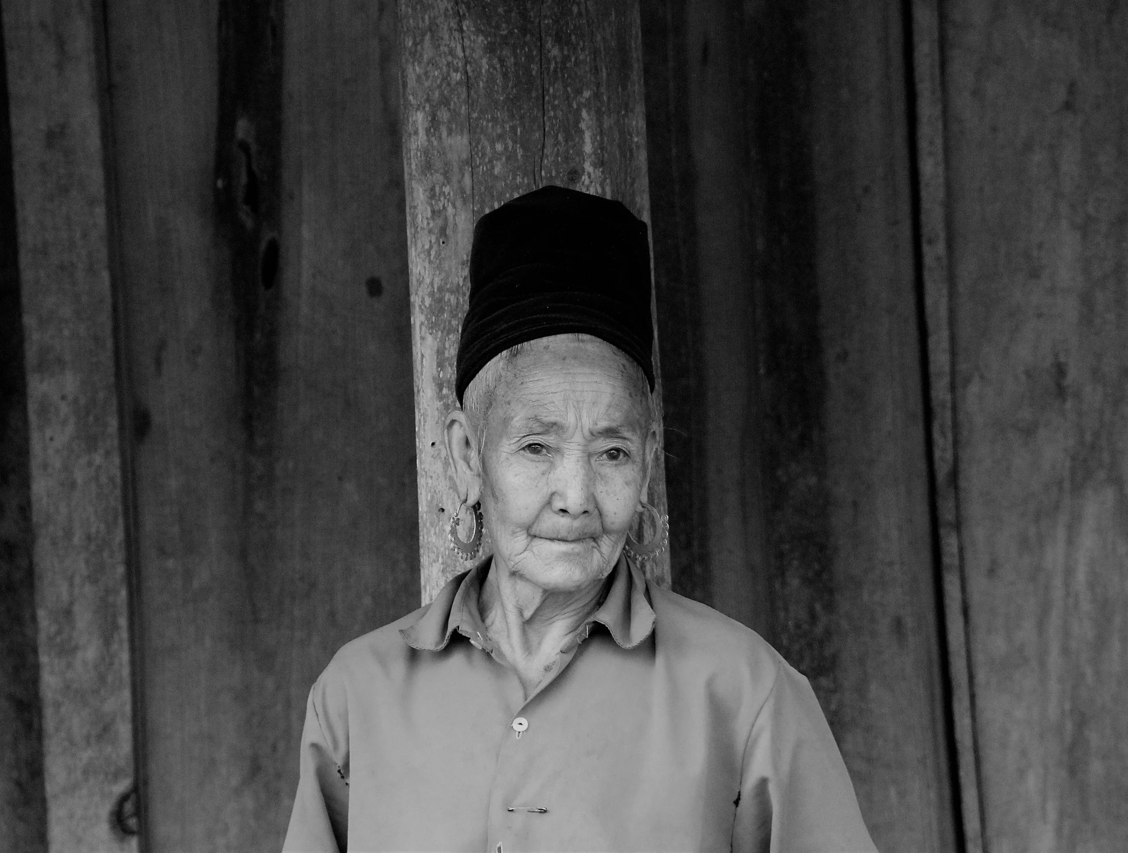 an old woman in a dress standing next to a wooden wall