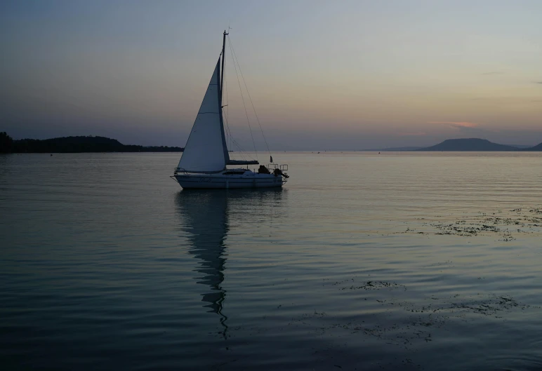sail boat with one person on water and mountain in distance