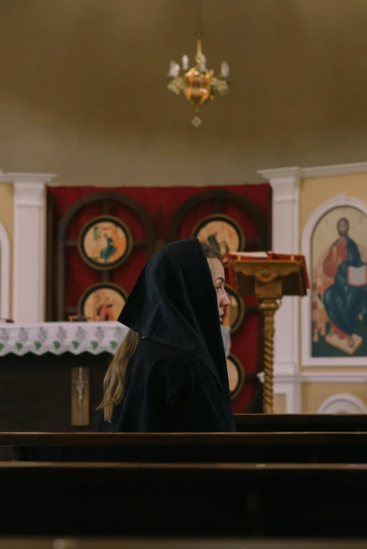 a woman in black sitting on a pew in front of a priest