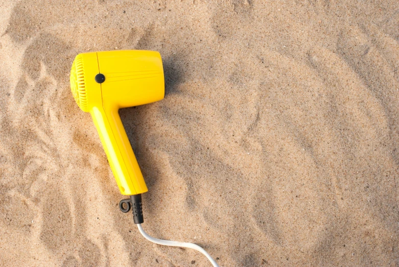 a yellow hair dryer sitting in the sand