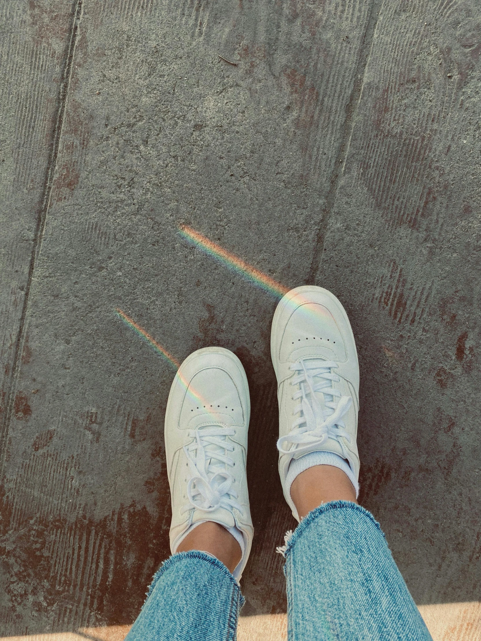 person with jeans and white sneakers and rainbow colored shoelaces