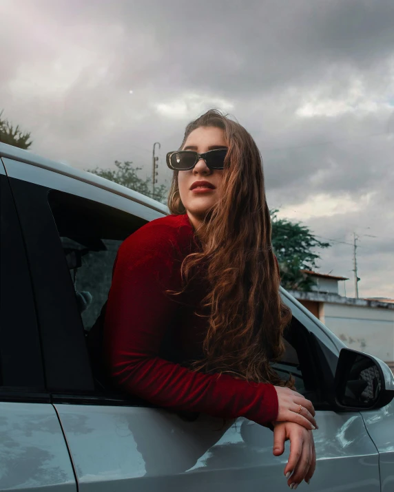 a woman is wearing sunglasses standing in the window of a car