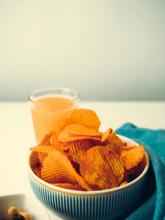 a bowl of chips next to a glass of orange juice