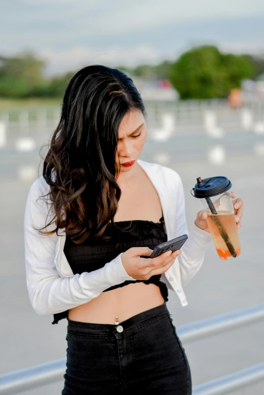 a woman looking at her cellphone while holding her cup of coffee