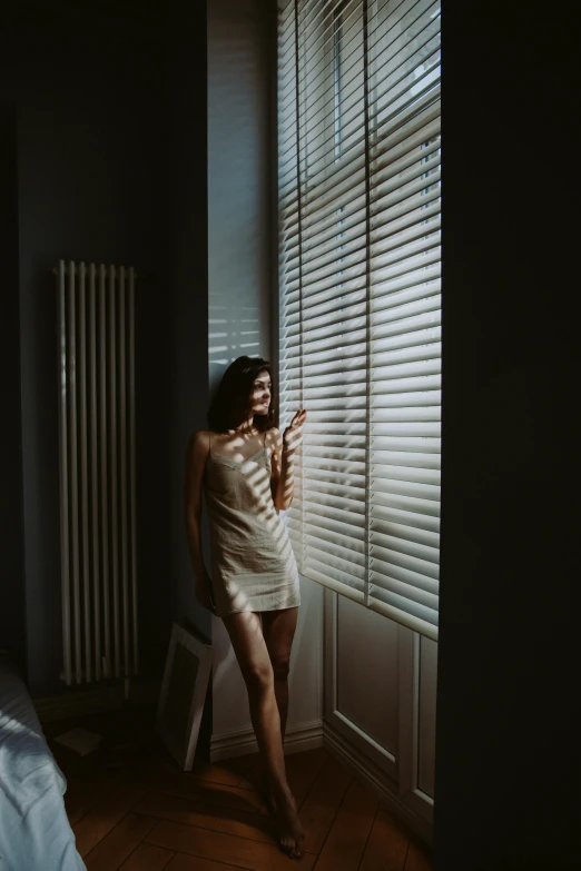 a woman standing in front of the blinds holding her cell phone