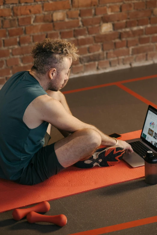 a man sitting on a mat with his laptop open