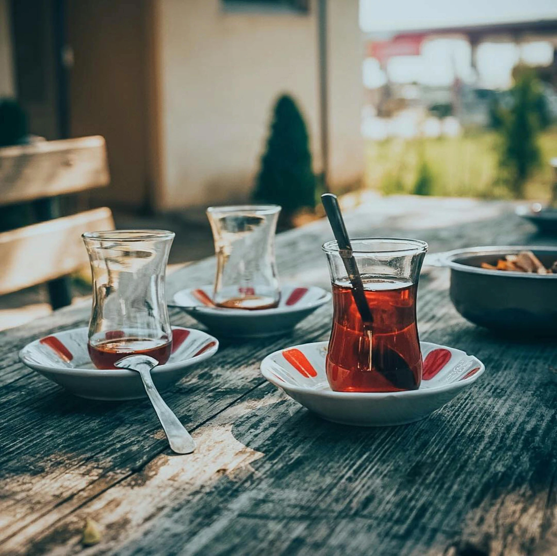 three glasses, a spoon and an empty cup on a wooden table outside