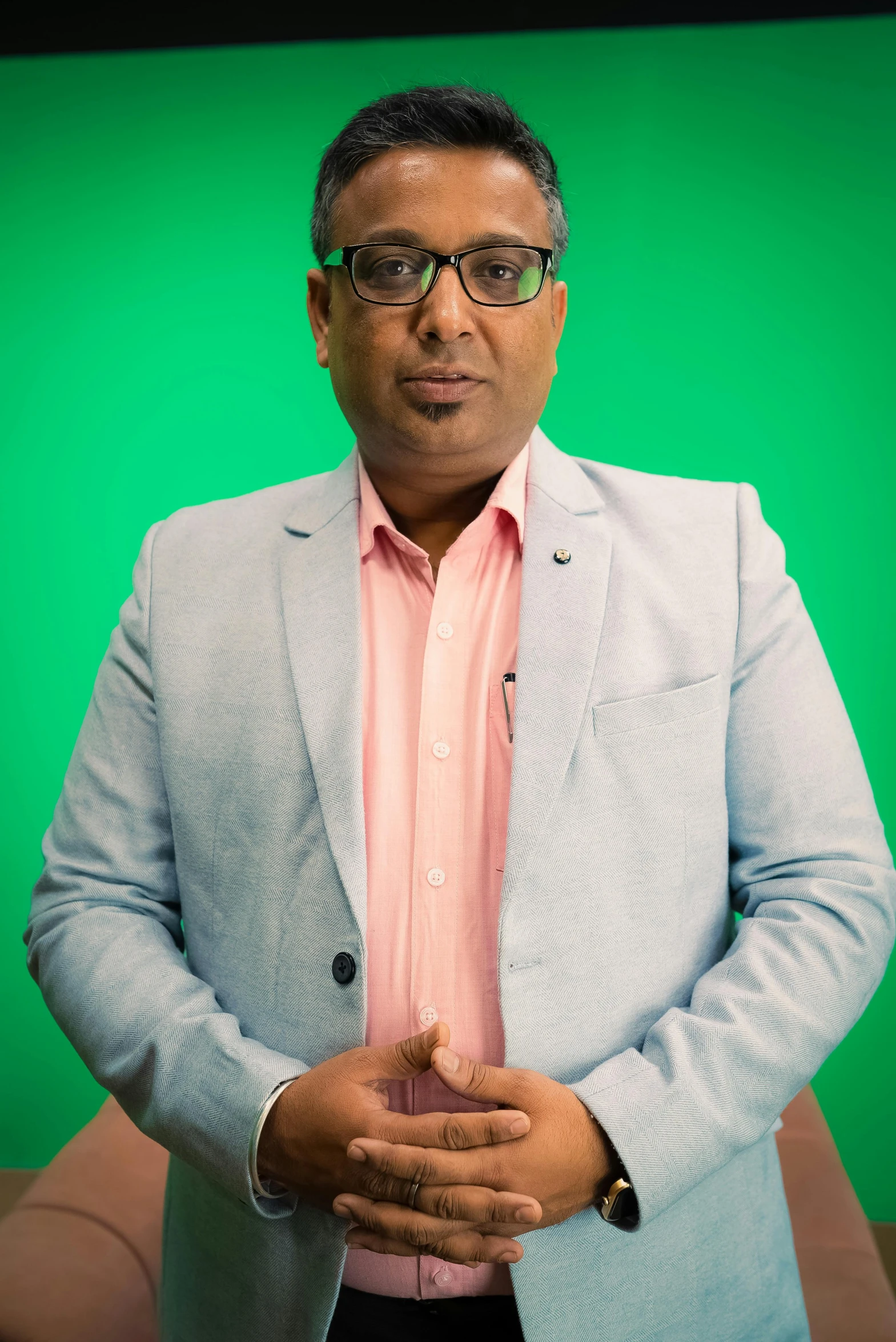 a man in a suit stands next to a green backdrop