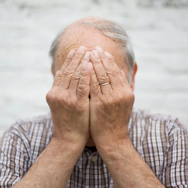 the man in plaid is covering his eyes with his hands