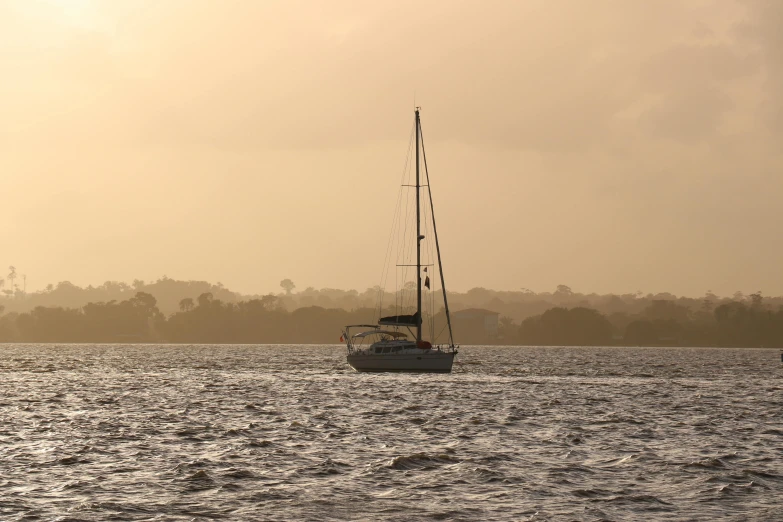 a sailboat sailing through a lake with hazy sky