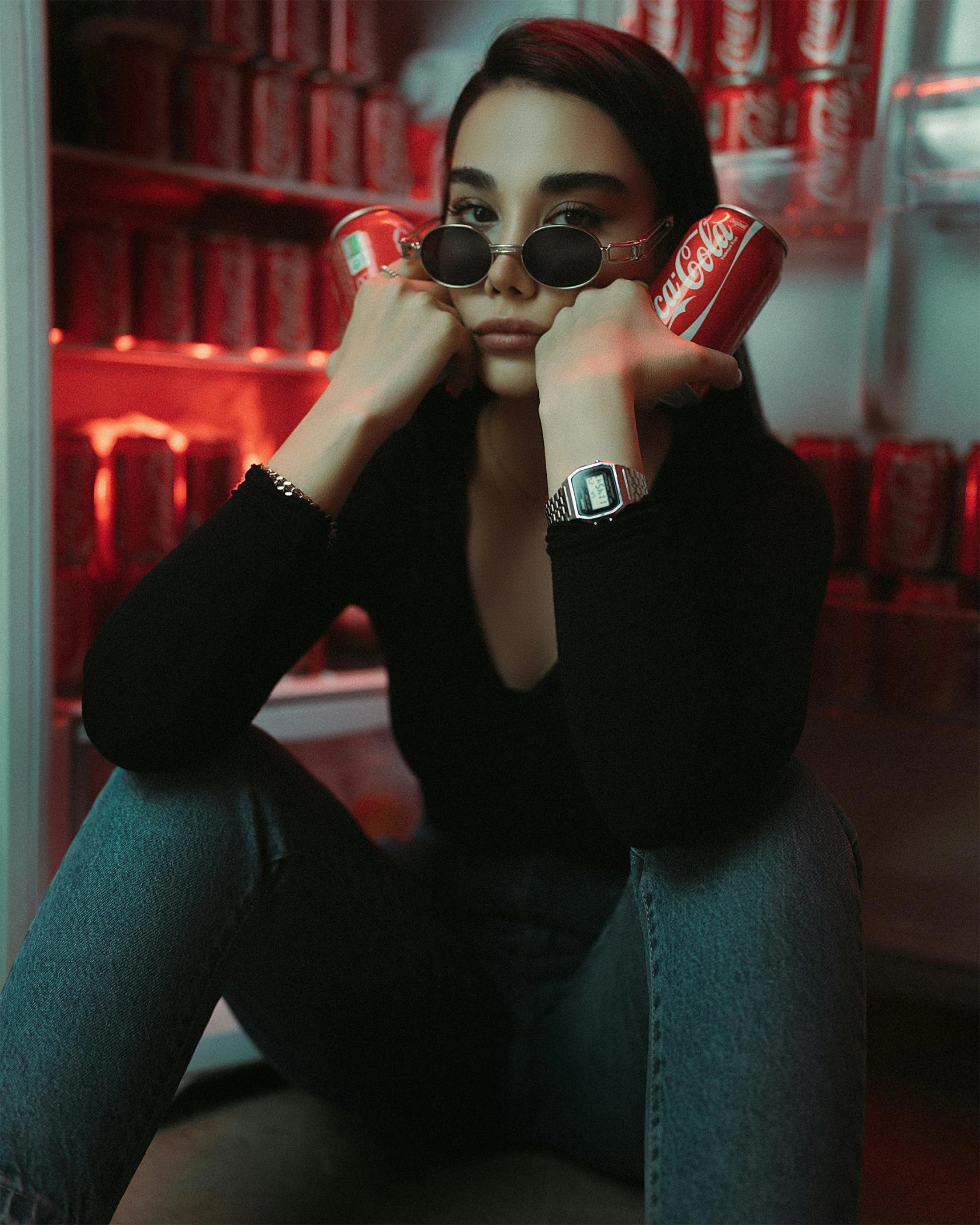 a young woman with glasses sits on a bench while holding up canisters