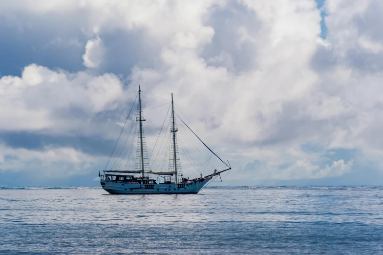 a blue boat in the ocean with clouds