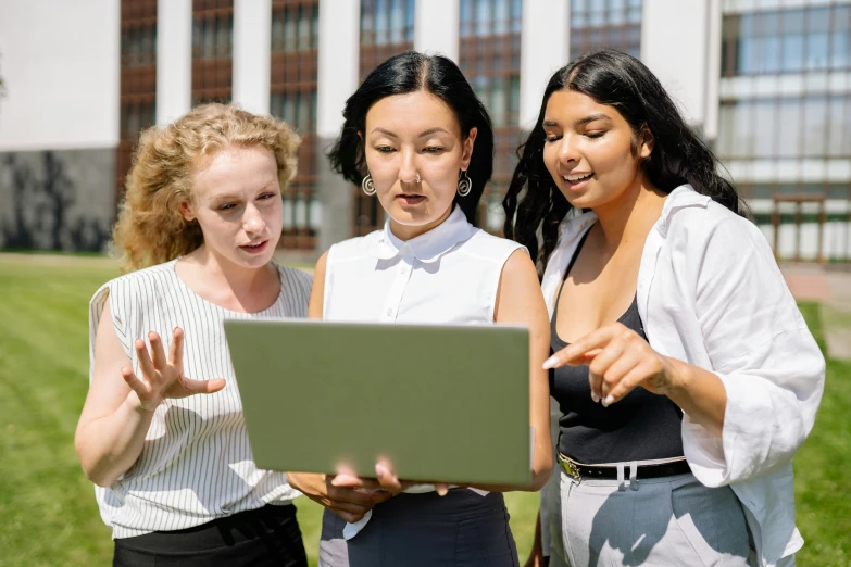 three women looking at a laptop outside