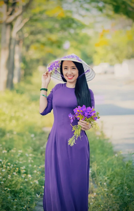 a woman in a dress and hat holds purple flowers