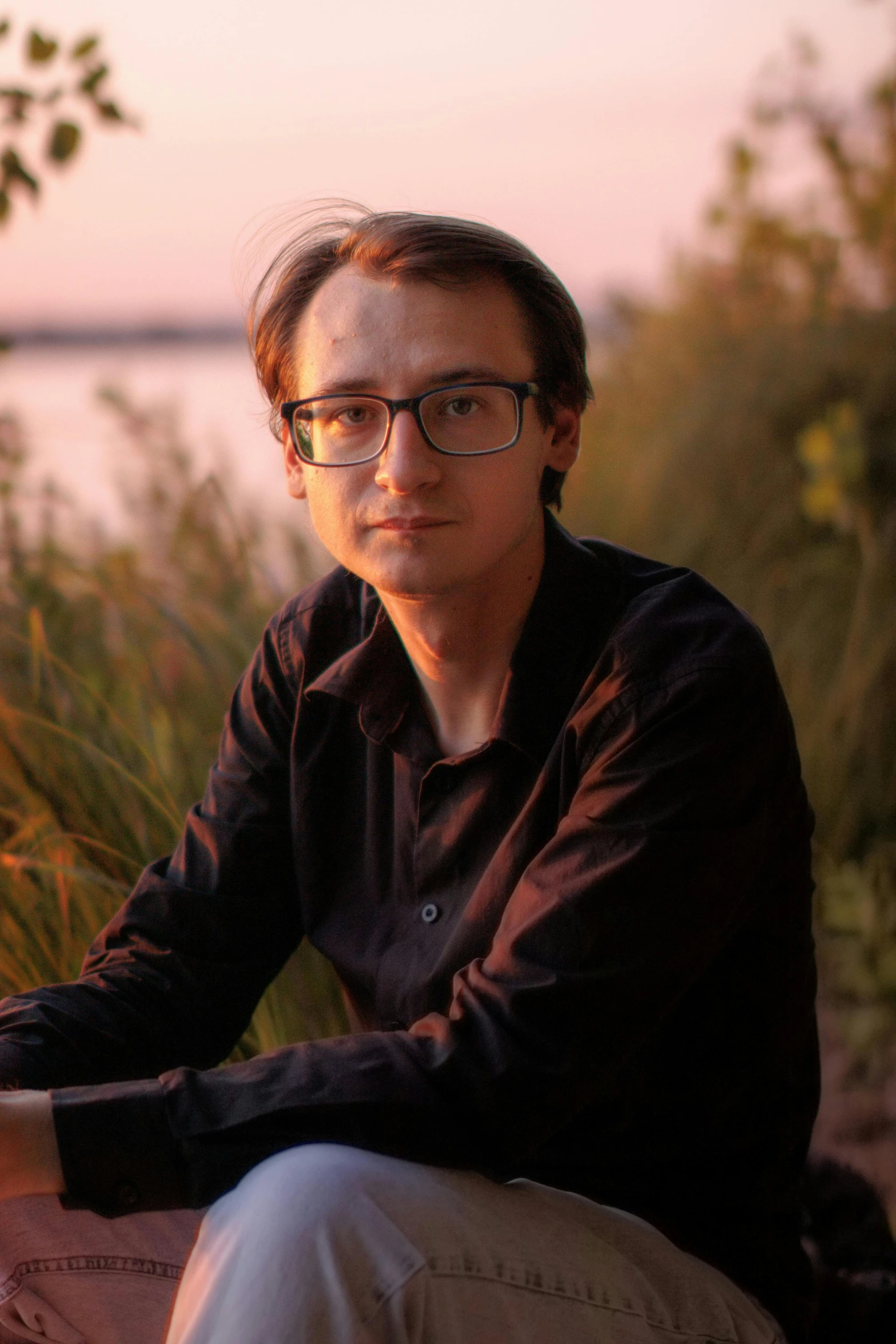 a man sits near water as the sun sets