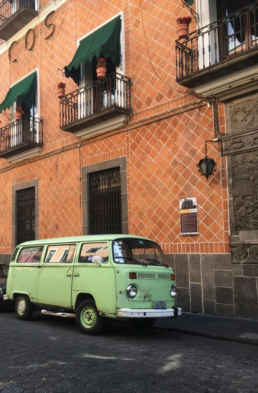 an old school green van parked in front of an orange building