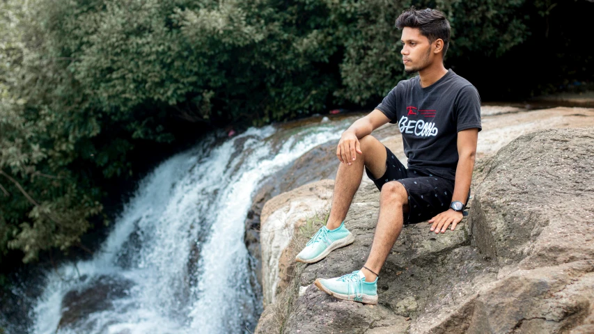 a man in blue and white sneakers sits on a rock near water