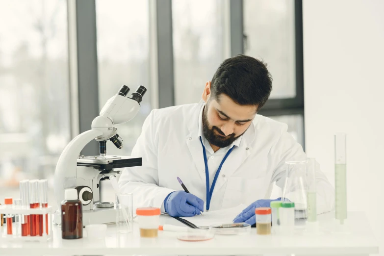 a man wearing a lab coat with gloves and holding a microscope in front of him and reading a notepad