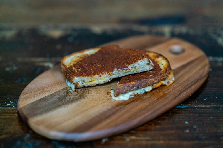 a grilled cheese sandwich sits on top of a wooden  board