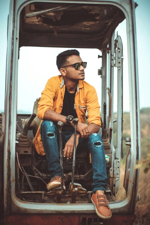 a man in orange jacket sitting on machinery near the side of a mountain