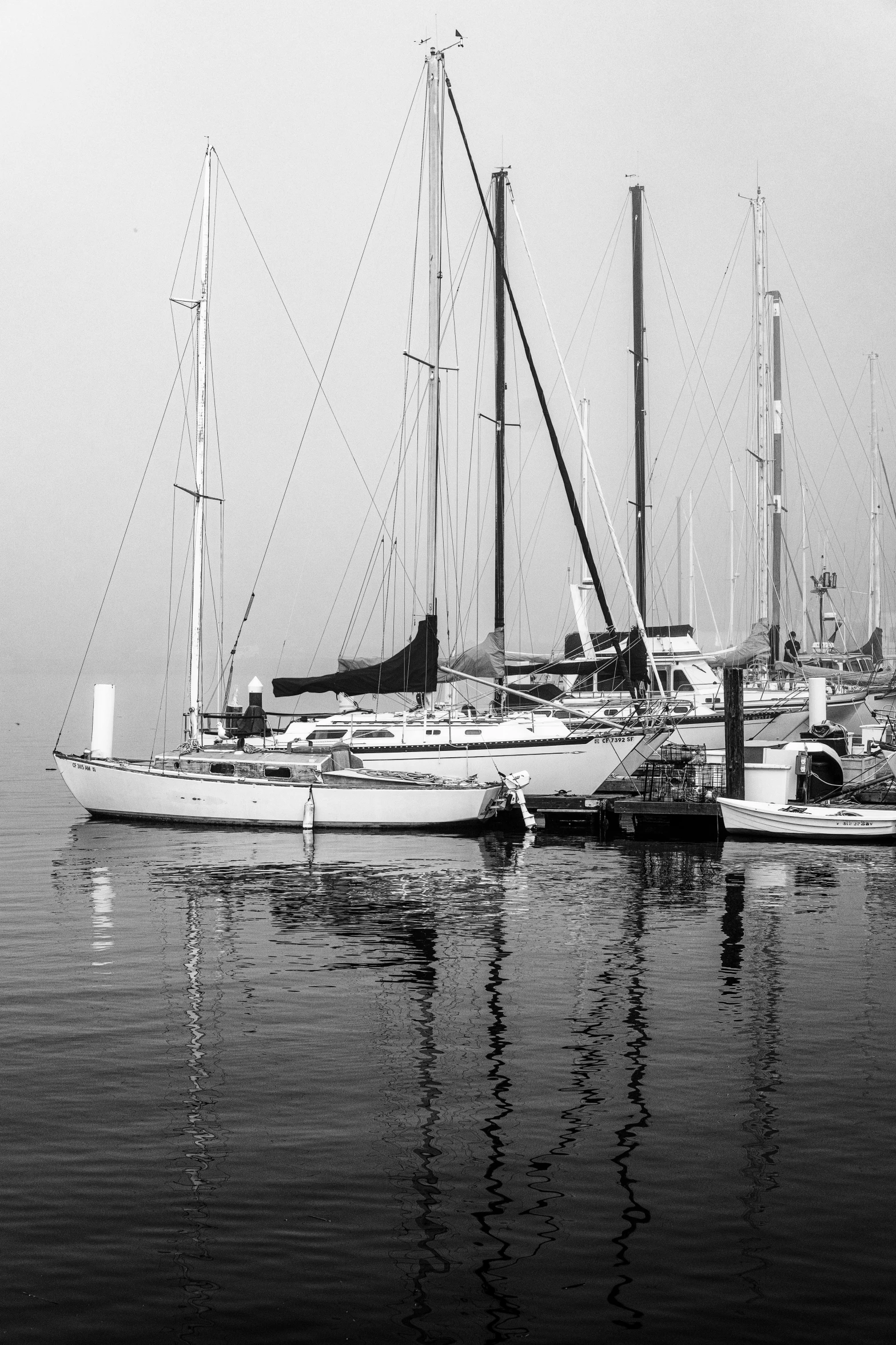 two sail boats in the water with a light fog