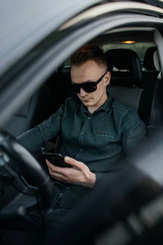 man in sunglasses sitting in car and texting on cellphone