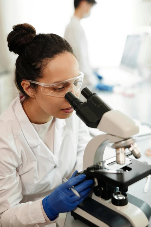 female scientist in white coat observing microscope in lab