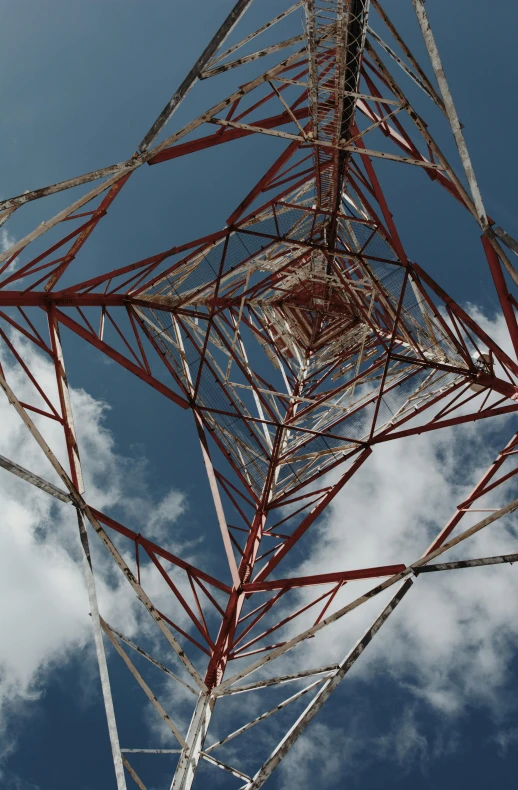 the top part of a tower structure with an electrical tower and clouds in the background