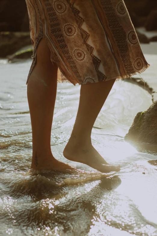 closeup image of woman standing on beach, water reflecting her feet