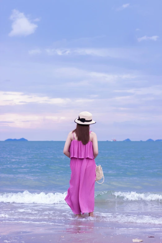 a woman with long hair in a wide legged pink dress walks along the beach