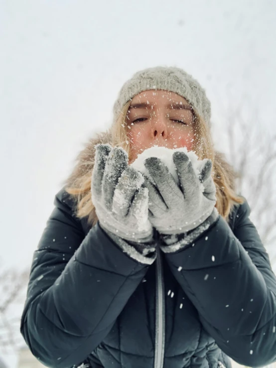 a woman that is wearing a winter jacket and has her hands under her face