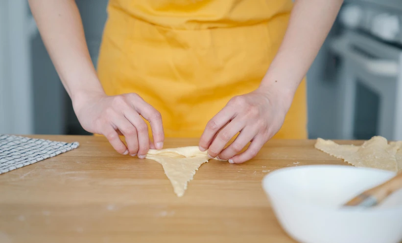 person in a yellow apron standing over a table making dough