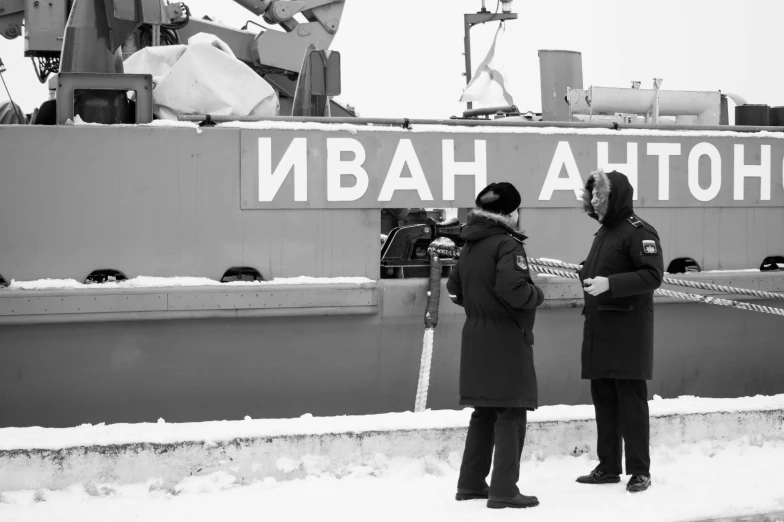 two people standing outside in the snow next to a boat