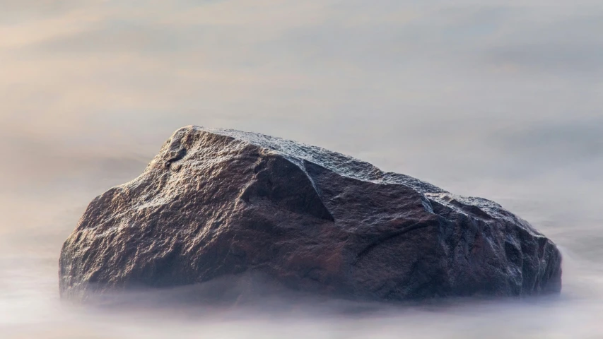 a rock in the ocean is submerged by clouds