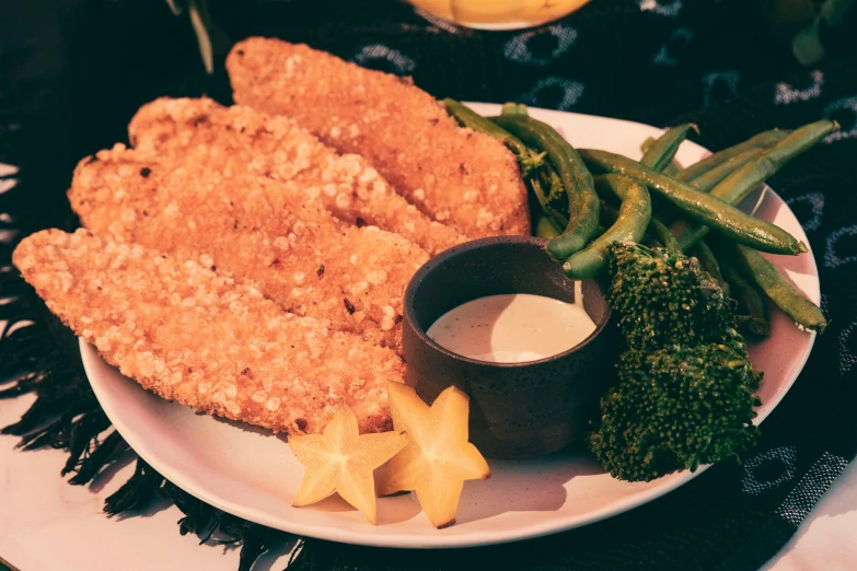 a plate topped with fried fish, broccoli and some beans