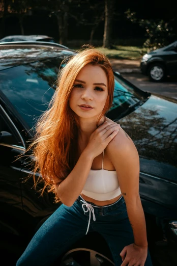 young woman leaning against car in street with trees in background