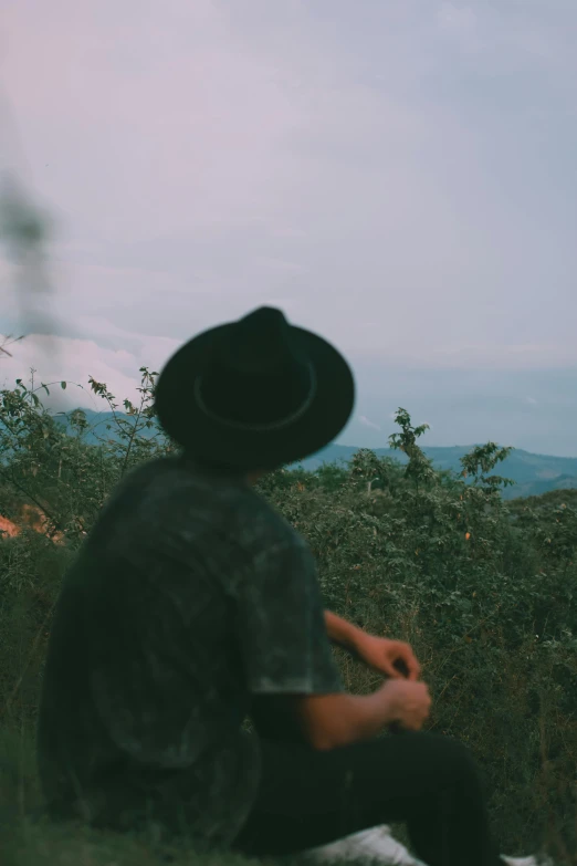 a lone man in a hat sits near the forest